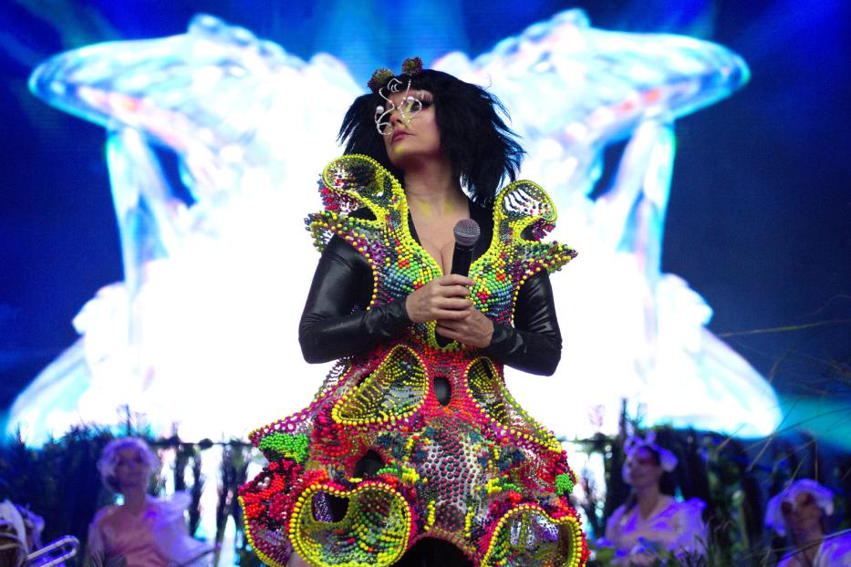 Björk tritt in einem farbenfrohen, extravaganten Kostüm auf einer Bühne auf.