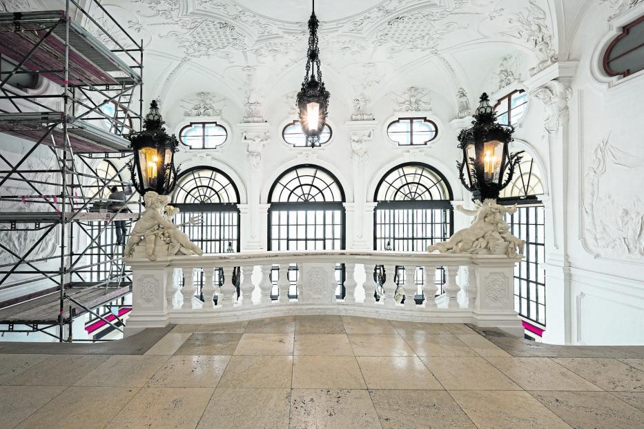 Blick auf eine kunstvolle Balustrade mit Skulpturen in einem prunkvollen, weißen Saal.