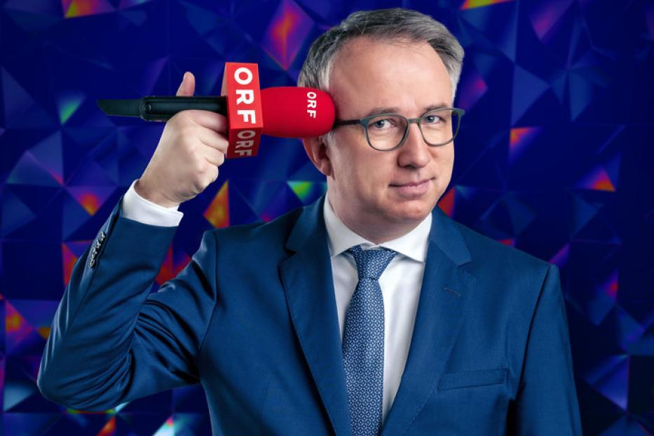 Ein Mann im Anzug hält ein rotes ORF-Mikrofon an seinen Kopf.