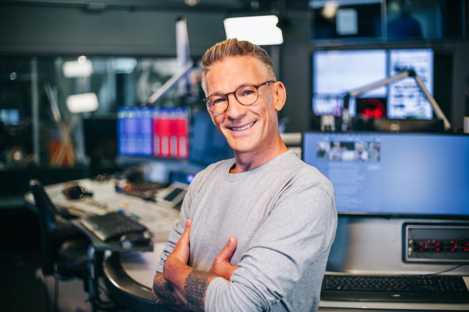 Ein Mann mit Brille lächelt in einem Radiostudio in die Kamera.