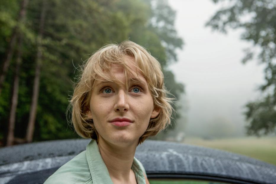 Eine junge Frau mit blonden Haaren und blauen Augen blickt nach oben.