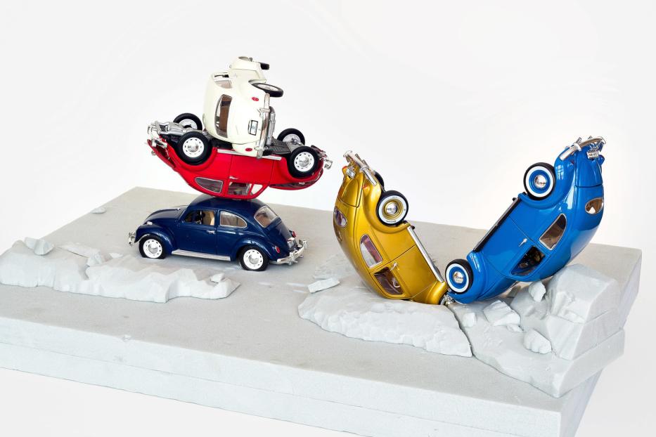 Mehrere Spielzeug-VW-Käfer sind auf einer grauen Oberfläche gestapelt und umgekippt.