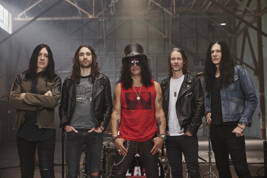 Die Rockband Slash posiert vor einem Schlagzeug in einer Lagerhalle.