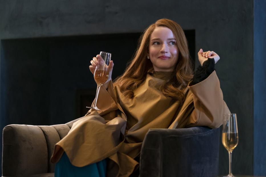 Julia Garner als Anna Delvey in der Netflix-Serie „Inventing Anna“ mit einem Champagnerglas in der Hand.