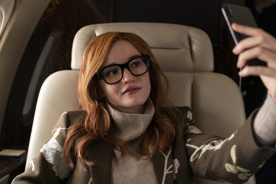 Eine Frau mit roten Haaren und Brille sitzt in einem Privatjet und macht ein Selfie.