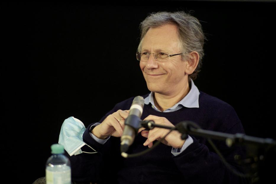 Ein Mann mit Brille lächelt und hält ein Mikrofon in den Händen.