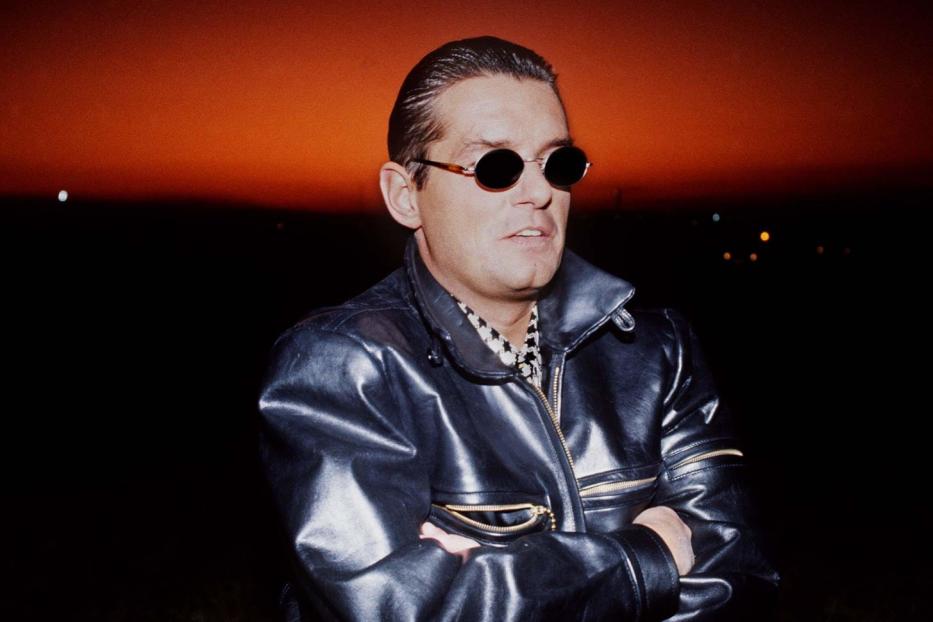 Ein Mann mit Sonnenbrille und Lederjacke vor einem orangefarbenen Himmel.