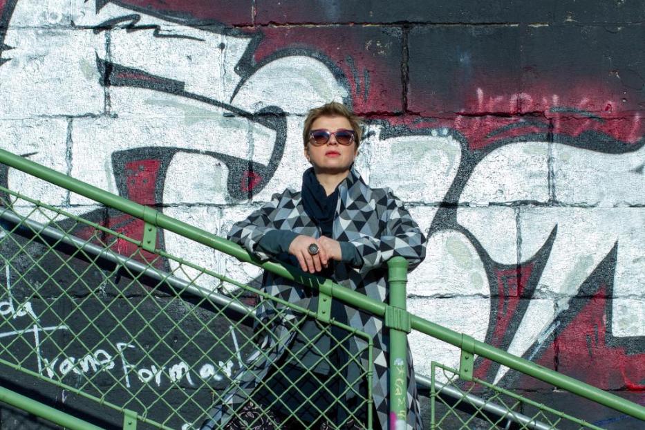 Eine Frau mit Sonnenbrille posiert auf einer Treppe vor einer Graffitiwand.