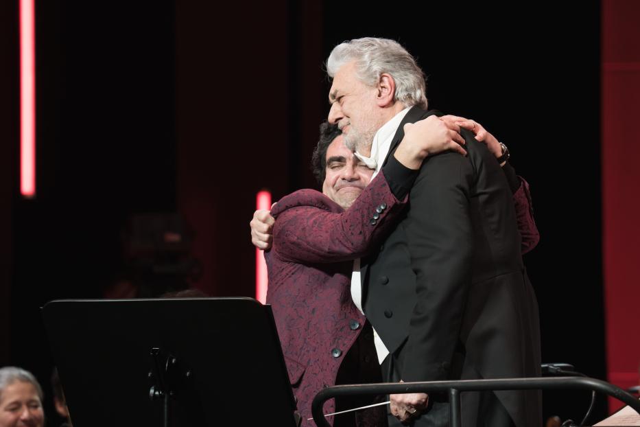 Plácido Domingo umarmt einen Dirigenten auf der Bühne.