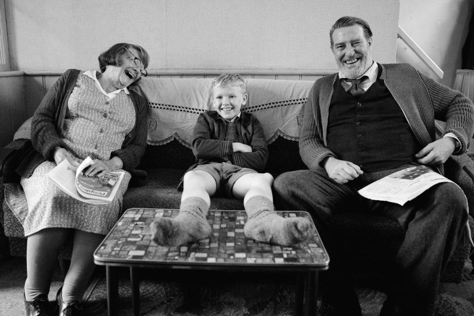 Schwarzweißaufnahme einer lachenden Familie, die auf einem Sofa sitzt.