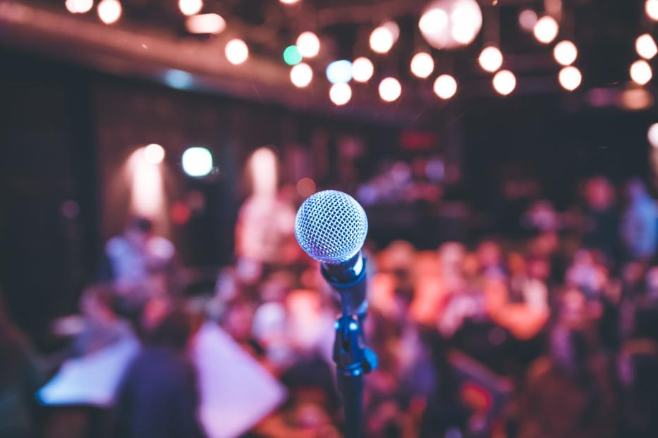 Event hall: Close up of microphone stand, seats with audience in the blurry background