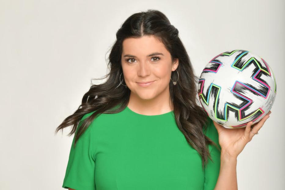 Eine Frau im grünen Oberteil hält einen Fußball in der Hand.