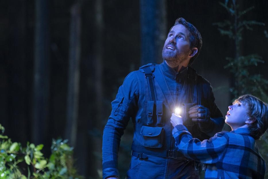Ryan Reynolds und ein Kind leuchten mit einer Taschenlampe in den Nachthimmel.