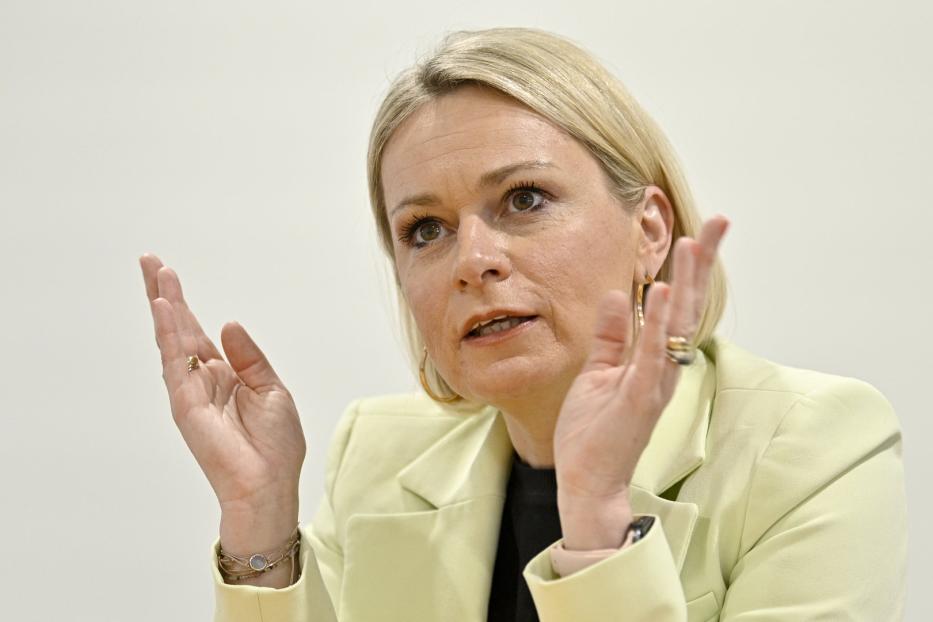Eine Frau in einem hellgrünen Blazer gestikuliert mit ihren Händen.