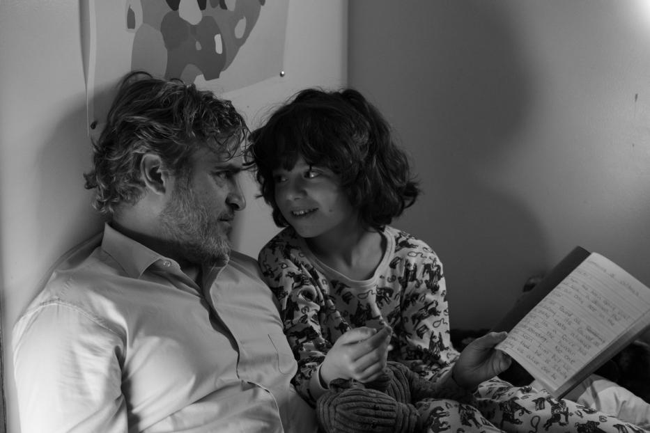 Joaquin Phoenix liest einem Kind im Bett eine Geschichte vor.