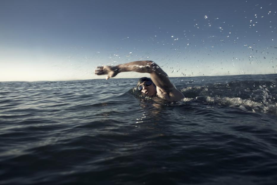 Ein Schwimmer mit Schwimmbrille krault im offenen Meer.