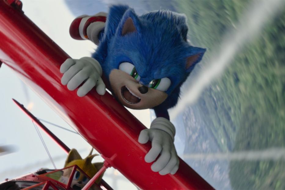 Sonic the Hedgehog hängt an einem roten Doppeldecker, während Tails das Flugzeug steuert.