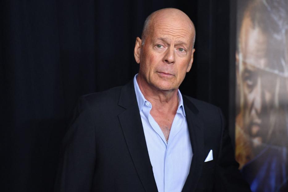 Bruce Willis posiert in einem schwarzen Anzug auf einem Event.