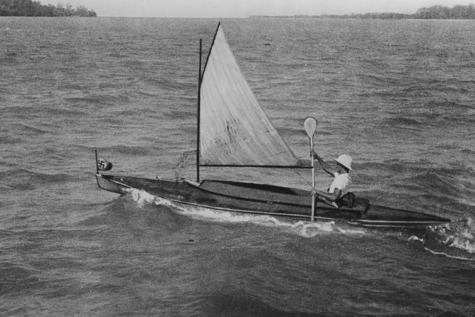 Eine Person segelt mit einem kleinen Segelboot, das eine Flagge mit einem Hakenkreuz trägt.