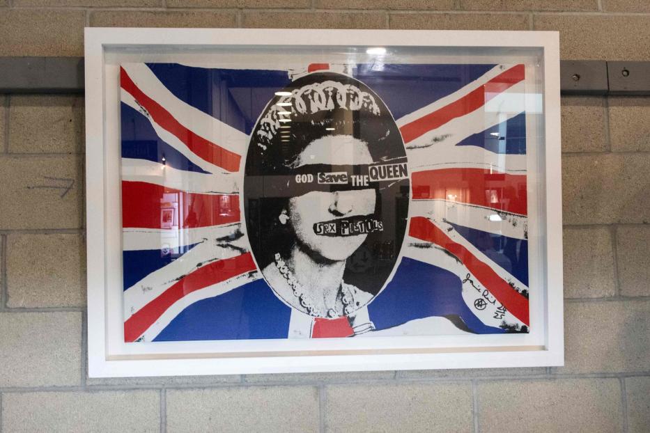 Ein gerahmtes Kunstwerk mit dem Motiv „God Save the Queen“ der Sex Pistols vor einer Union-Jack-Flagge.