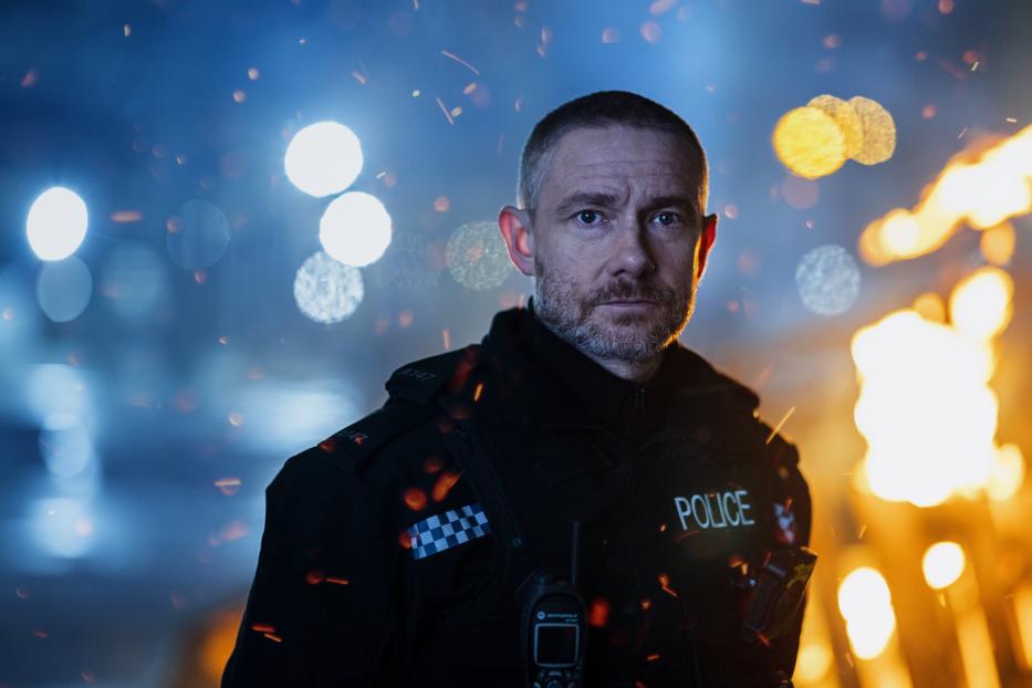 Ein Polizist steht vor einem Hintergrund aus Lichtern und Flammen.