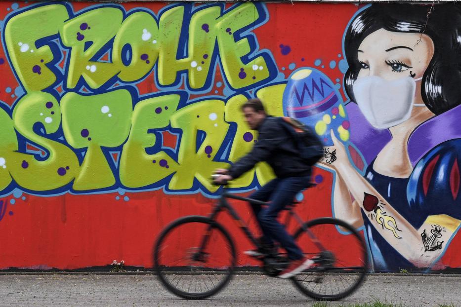 Ein Radfahrer fährt an einem Graffiti vorbei, das „Frohe Ostern“ und Schneewittchen mit Maske zeigt.