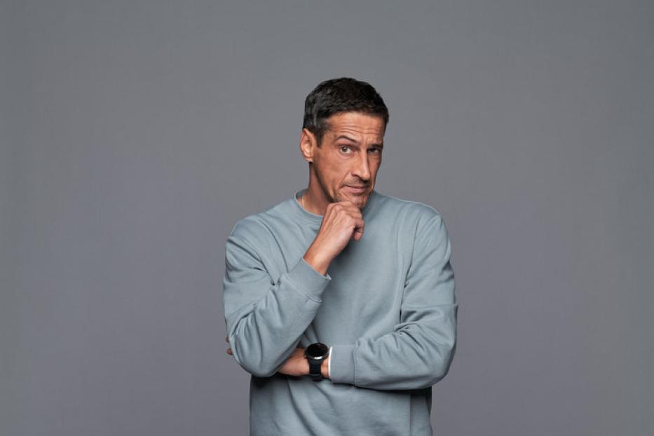 Ein Mann in Jeans, Pullover und Turnschuhen steht nachdenklich da.