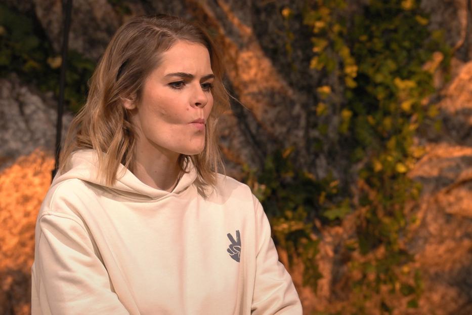 Eine Frau mit blonden Haaren und einem Kapuzenpullover mit Friedenszeichen vor einem Felsen.