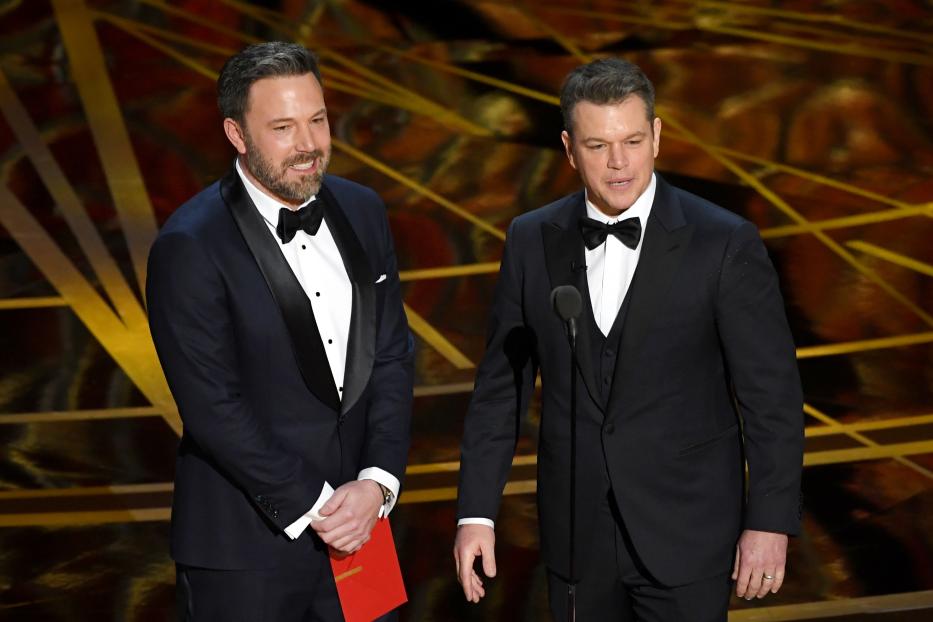 Ben Affleck und Matt Damon in Anzügen auf einer Bühne.