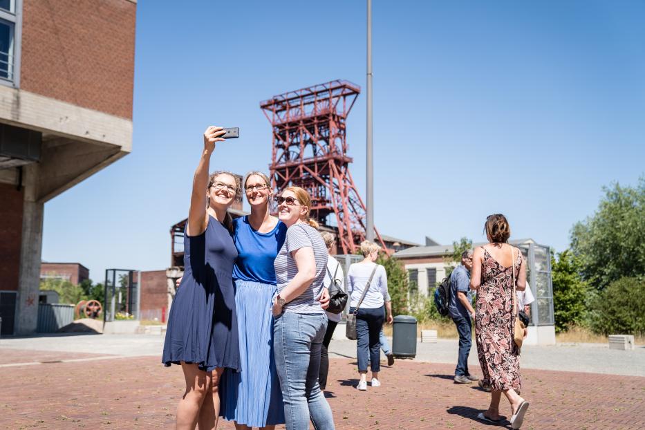 Drei Frauen machen ein Selfie vor einem Förderturm auf dem Gelände Zollverein in Essen.