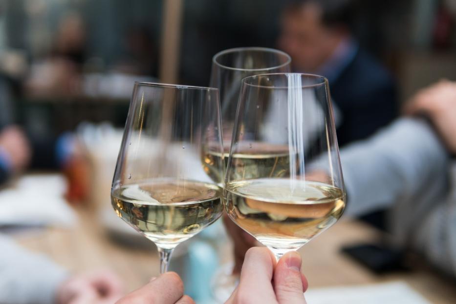 Drei Gläser Weißwein werden bei einer Feier angestoßen.