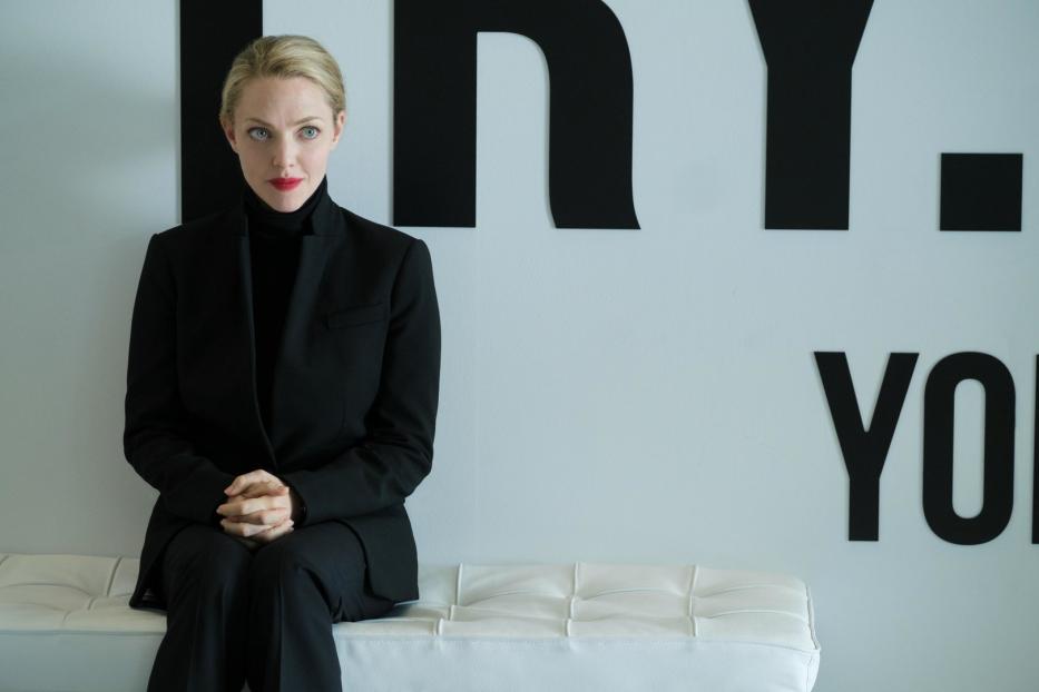 Amanda Seyfried sitzt in einem schwarzen Hosenanzug vor einer Wand mit schwarzen Buchstaben.