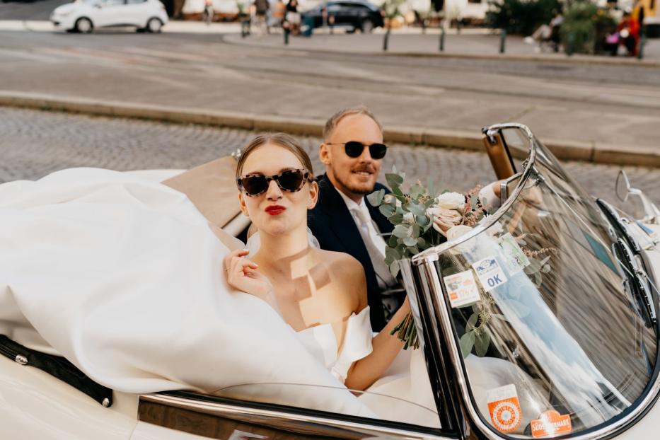 Ein Brautpaar fährt in einem Oldtimer-Cabriolet durch die Stadt.