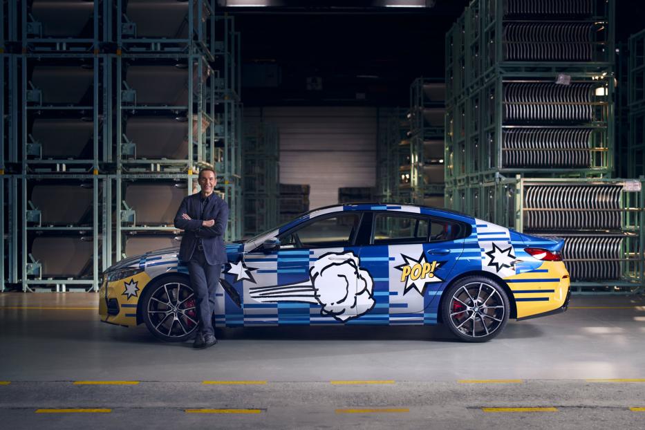 Ein Mann posiert vor einem BMW mit Pop-Art-Design in einer Lagerhalle.