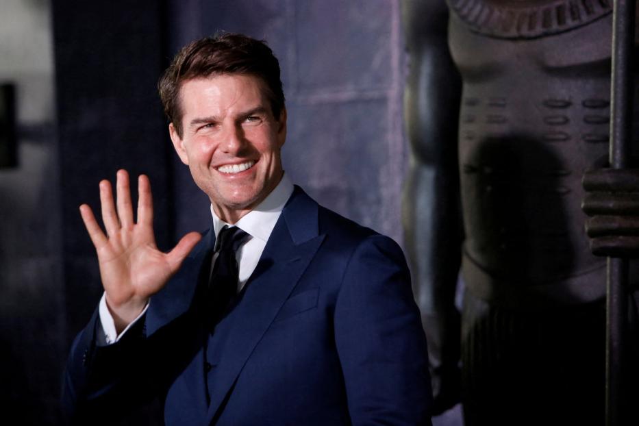 Tom Cruise lächelt und winkt in einem blauen Anzug.