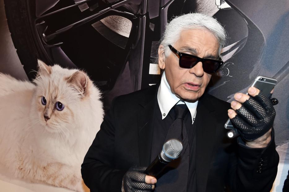 Karl Lagerfeld mit Mikrofon und Smartphone vor einem Bild seiner Katze Choupette.