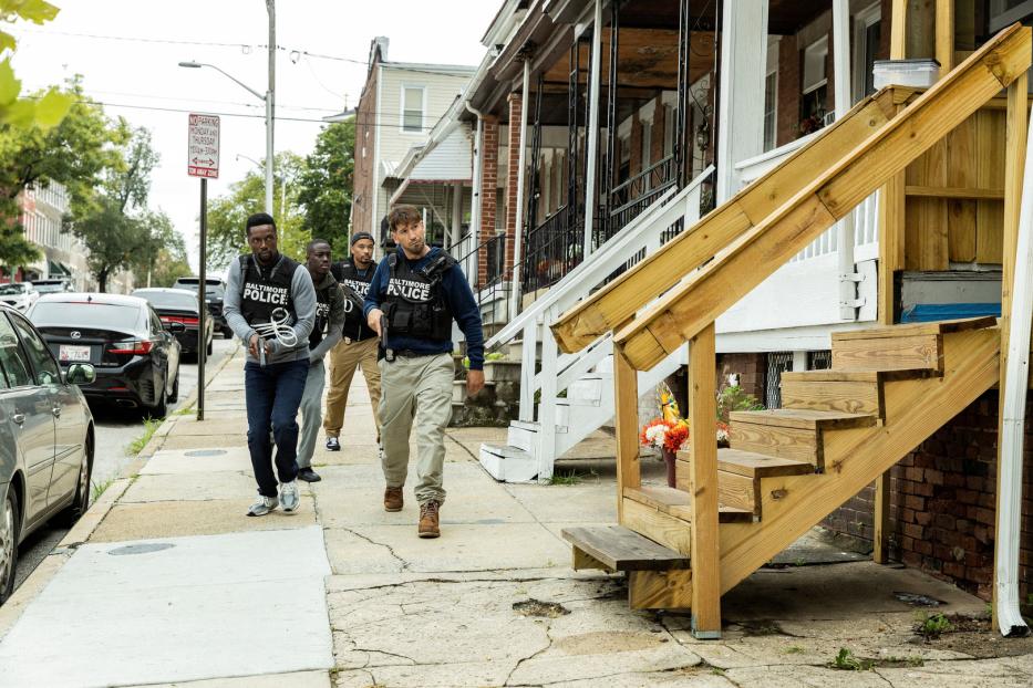 Mehrere Polizisten in kugelsicheren Westen mit der Aufschrift „Baltimore Police“ gehen auf einem Bürgersteig entlang.