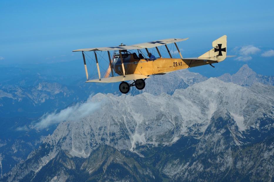 Ein historisches gelbes Flugzeug fliegt über eine Berglandschaft.