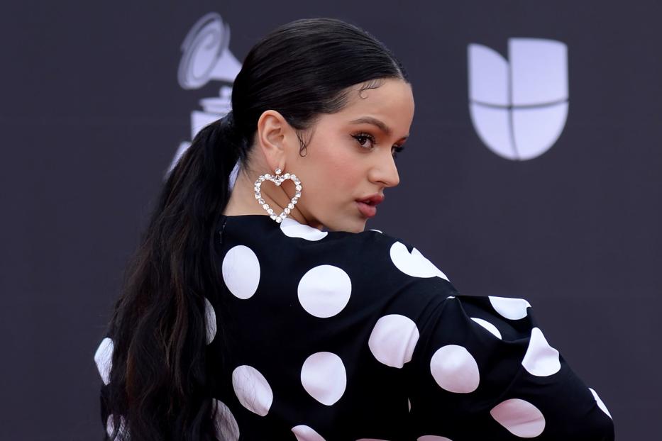 Rosalía trägt ein schwarz-weiß gepunktetes Kleid und herzförmige Ohrringe.