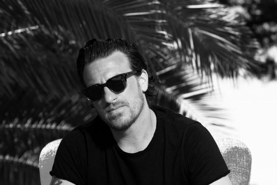 Ein Mann mit Sonnenbrille sitzt in einem Sessel vor einer Palme.