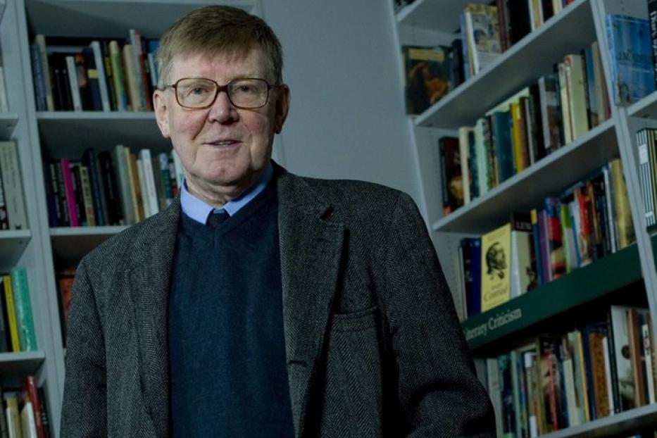 Ein Mann mit Brille und Jackett steht vor einem Bücherregal.