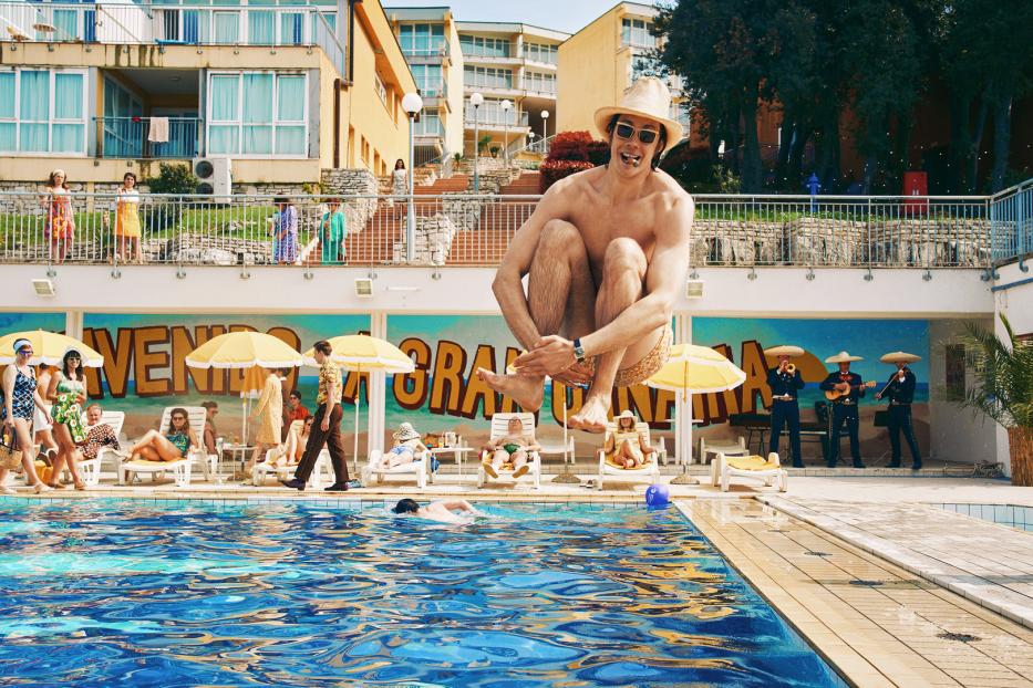 Ein Mann schwebt über einem Pool, während andere sich sonnen und eine Mariachi-Band spielt.