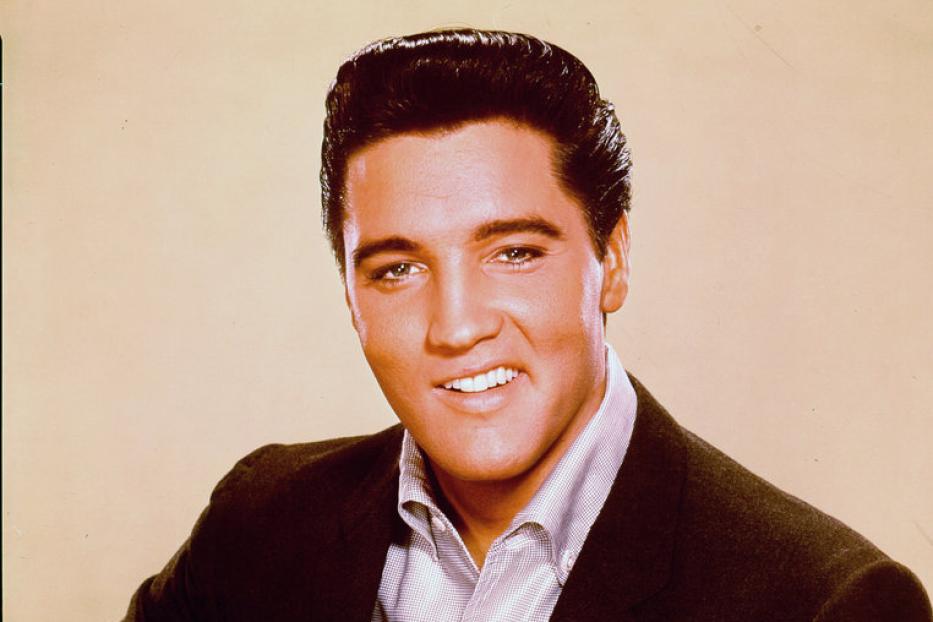 Elvis Presley mit Gitarre in einem dunklen Anzug.