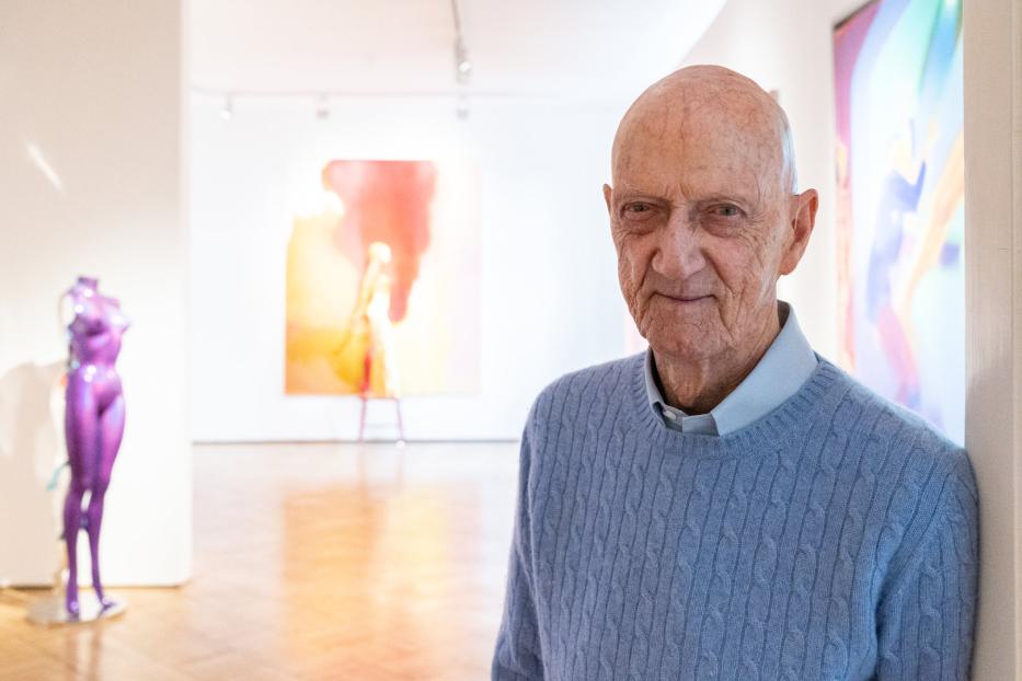 Ein älterer Mann steht in einer Kunstgalerie vor abstrakten Gemälden und einer lila Skulptur.