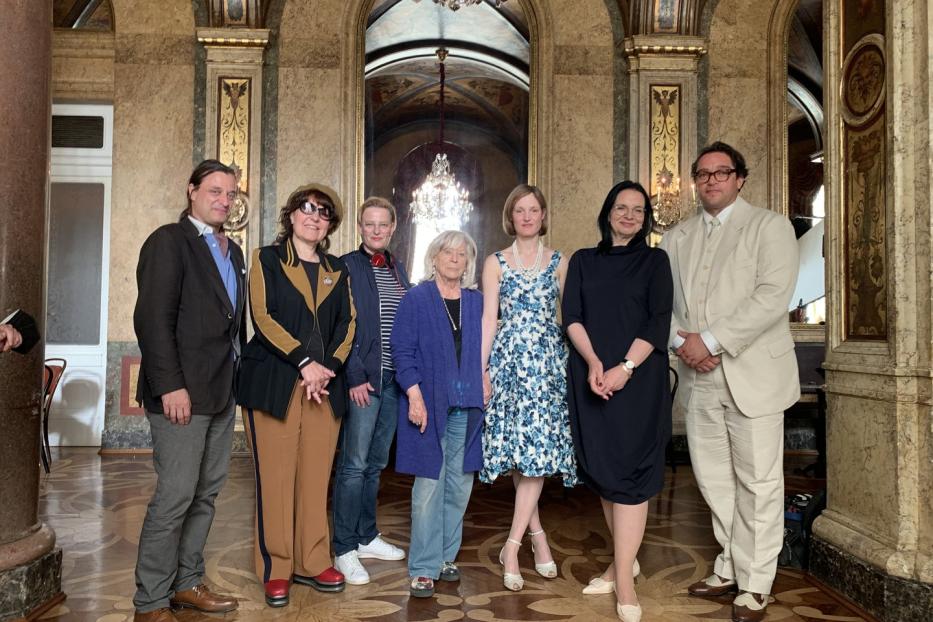 Eine Gruppe von sieben Personen posiert in einem opulenten Saal für ein Foto.
