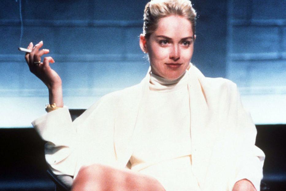 Sharon Stone sitzt mit einer Zigarette in der Hand auf einem Stuhl.