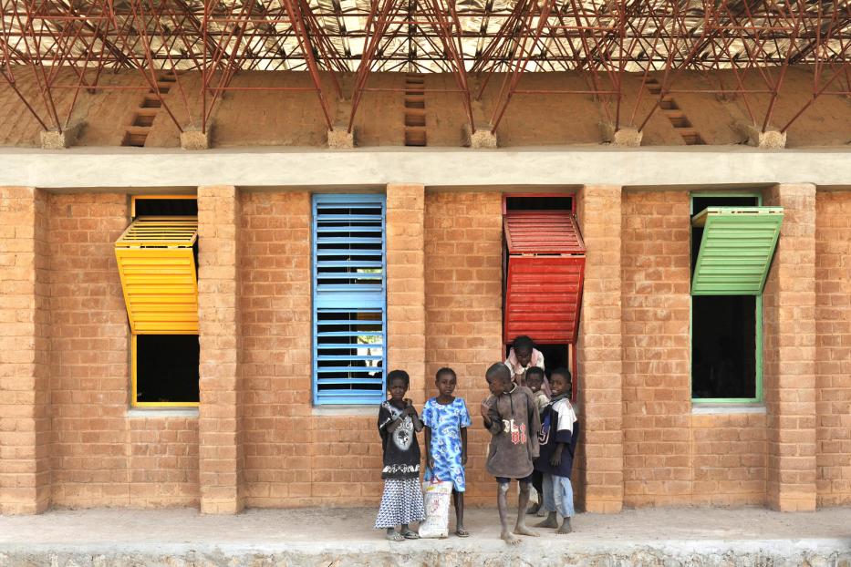 Eine Gruppe Kinder steht vor einem Backsteingebäude mit farbigen Fensterläden.