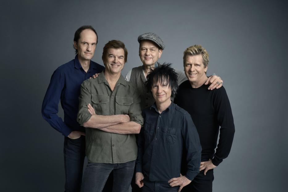 Die deutsche Rockband Die Ärzte posiert vor einem grauen Hintergrund.