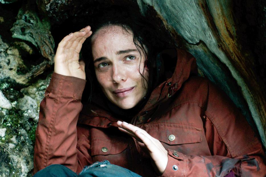 Eine Frau mit schmutzigem Gesicht und Jacke kauert in einer Felsspalte.