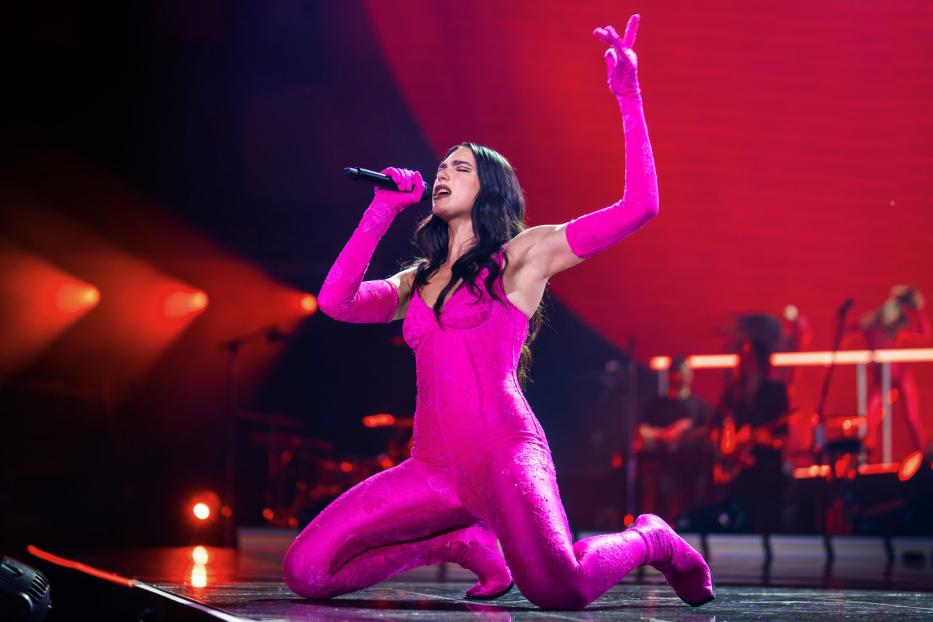 Dua Lipa kniet auf der Bühne und singt in einem pinkfarbenen Outfit.